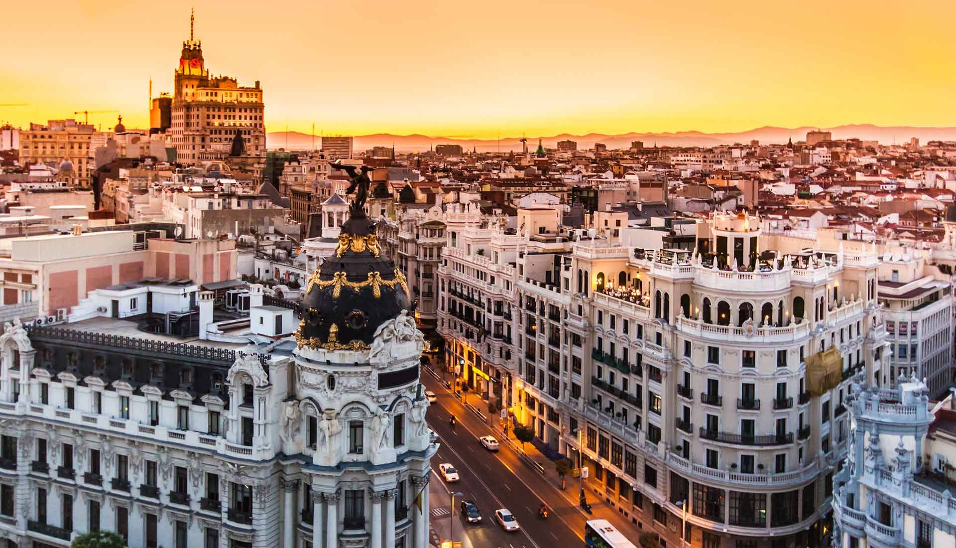 Puesta de sol sobre el horizonte de Madrid con el edificio Metrópolis iluminado y la calle Gran Vía abajo.